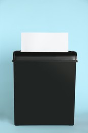 Photo of Shredder with sheet of white paper on light blue background