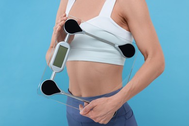 Photo of Slim woman holding scales on light blue background, closeup. Weight loss