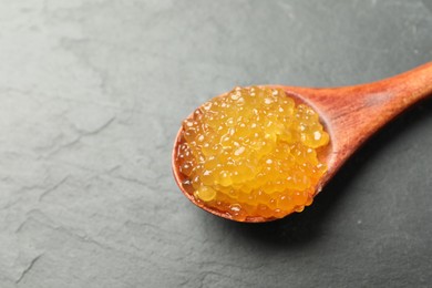 Photo of Fresh pike caviar in spoon on black table, closeup. Space for text