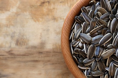 Photo of Bowl with organic sunflower seeds on wooden table, top view. Space for text