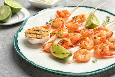 Photo of Plate with delicious fried shrimp skewers and lime on grey background, closeup