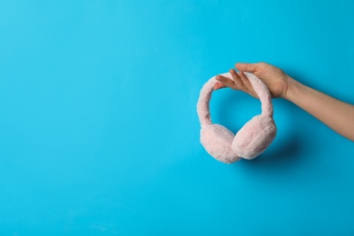 Photo of Woman holding stylish winter earmuffs on light blue background, closeup. Space for text