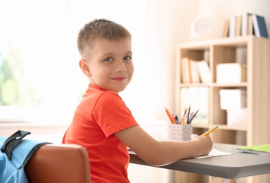 Photo of Cute little child doing assignment at desk in classroom. Elementary school