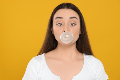 Photo of Beautiful young woman blowing bubble gum on yellow background