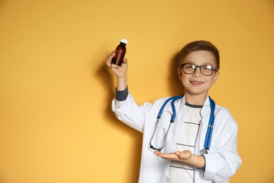 Photo of Cute little child in doctor coat with medication on color background. Space for text