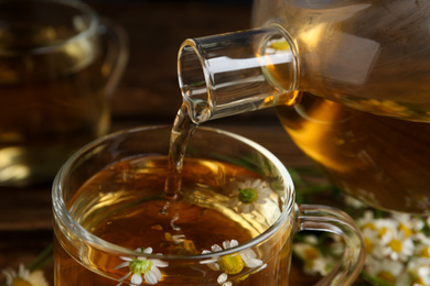 Photo of Pouring tasty chamomile tea into glass cup on  table, closeup