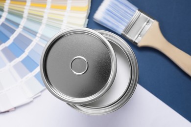 Photo of Can with white paint, brush and color palette on blue background, flat lay