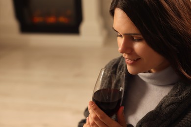 Photo of Young woman with glass of wine resting near fireplace indoors, closeup. Space for text