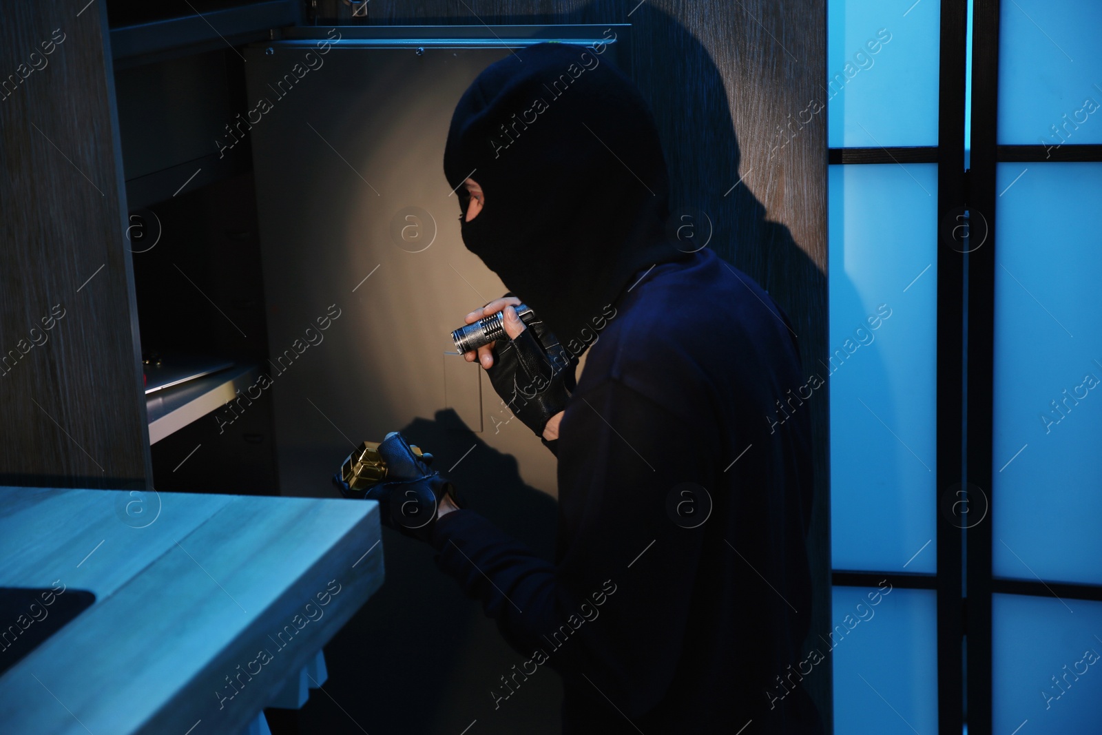 Photo of Thief taking gold bars out of steel safe indoors at night