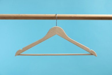 Photo of Empty clothes hanger on wooden rack against light blue background