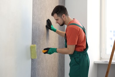 Man hanging stylish gray wallpaper in room