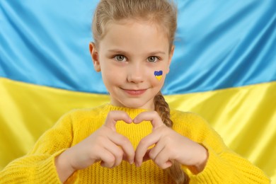 Photo of Little girl making heart with her hands near Ukrainian flag