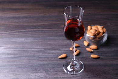 Photo of Liqueur glass with tasty amaretto and almonds on wooden table, space for text