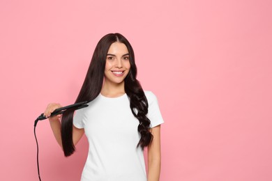 Photo of Beautiful happy woman using hair iron on pink background. Space for text
