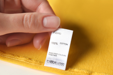 Photo of Woman reading clothing label with care symbols and material content on yellow shirt, closeup