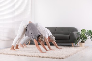 Photo of Senior couple practicing yoga on carpet at home. Healthy lifestyle