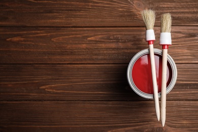 Photo of Open can with paint and brushes on wooden table, top view