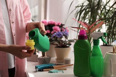 Photo of Woman pouring liquid fertilizer to take care of house plants indoors, closeup