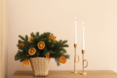 Photo of Wicker basket with fir tree branches and dried orange slices on wooden table near beige wall. Decor for stylish interior
