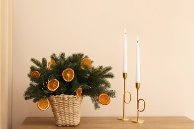 Wicker basket with fir tree branches and dried orange slices on wooden table near beige wall. Decor for stylish interior