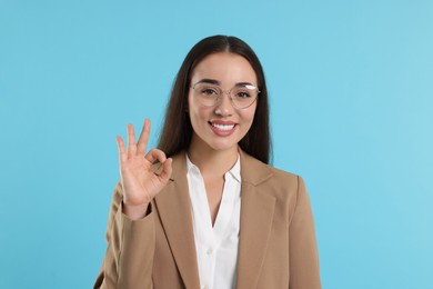 Photo of Beautiful woman in glasses showing OK gesture on turquoise background