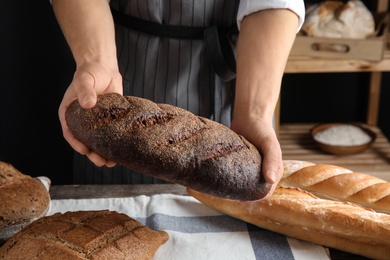 Photo of Baker holding loaf of bread over table indoors, closeup