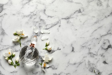 Photo of Bottle of luxury perfume and fresh jasmine flowers on white marble table, flat lay. Space for text