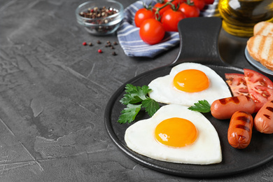 Photo of Delicious breakfast with heart shaped fried eggs and sausages on dark grey table. Space for text