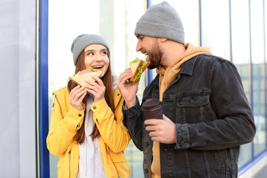 Photo of Happy young couple with sandwiches and coffee on city street