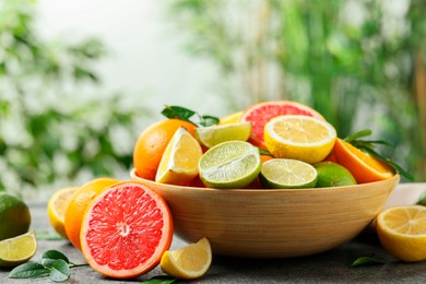 Photo of Different fresh citrus fruits and leaves on table against blurred background, closeup