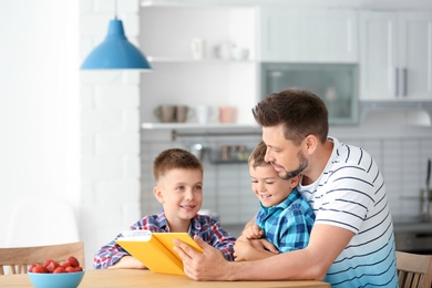 Photo of Dad and his sons reading interesting book in kitchen. Space for text