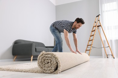 Photo of Man unrolling new clean carpet in room