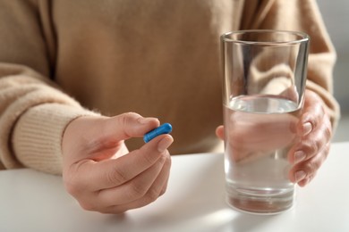 Photo of Woman with glass of water and pill at white table, closeup