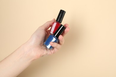 Photo of Woman holding nail polishes on beige background, closeup