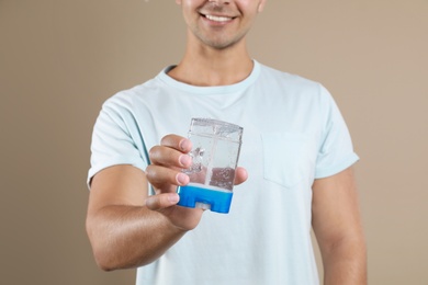 Young man holding deodorant on beige background, closeup. Mockup for design