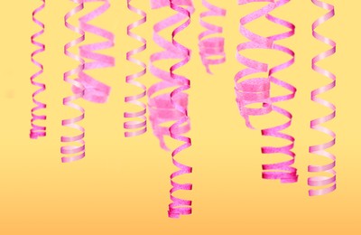 Image of Many pink serpentine streamers on yellow background. Party decor