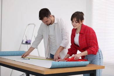 Photo of Woman and man applying glue onto wallpaper sheet at wooden table indoors