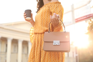 Photo of Young woman with stylish brown bag and cup of coffee on city street, closeup