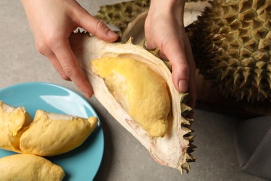 Photo of Woman with piece of fresh durian at grey table, top view